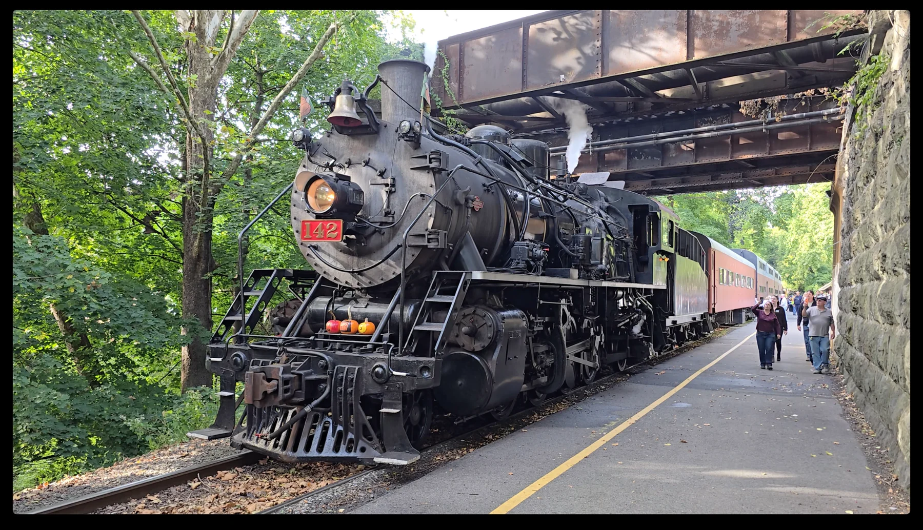 Steam locomotive 142 with passenger cars beneath a steel bridge